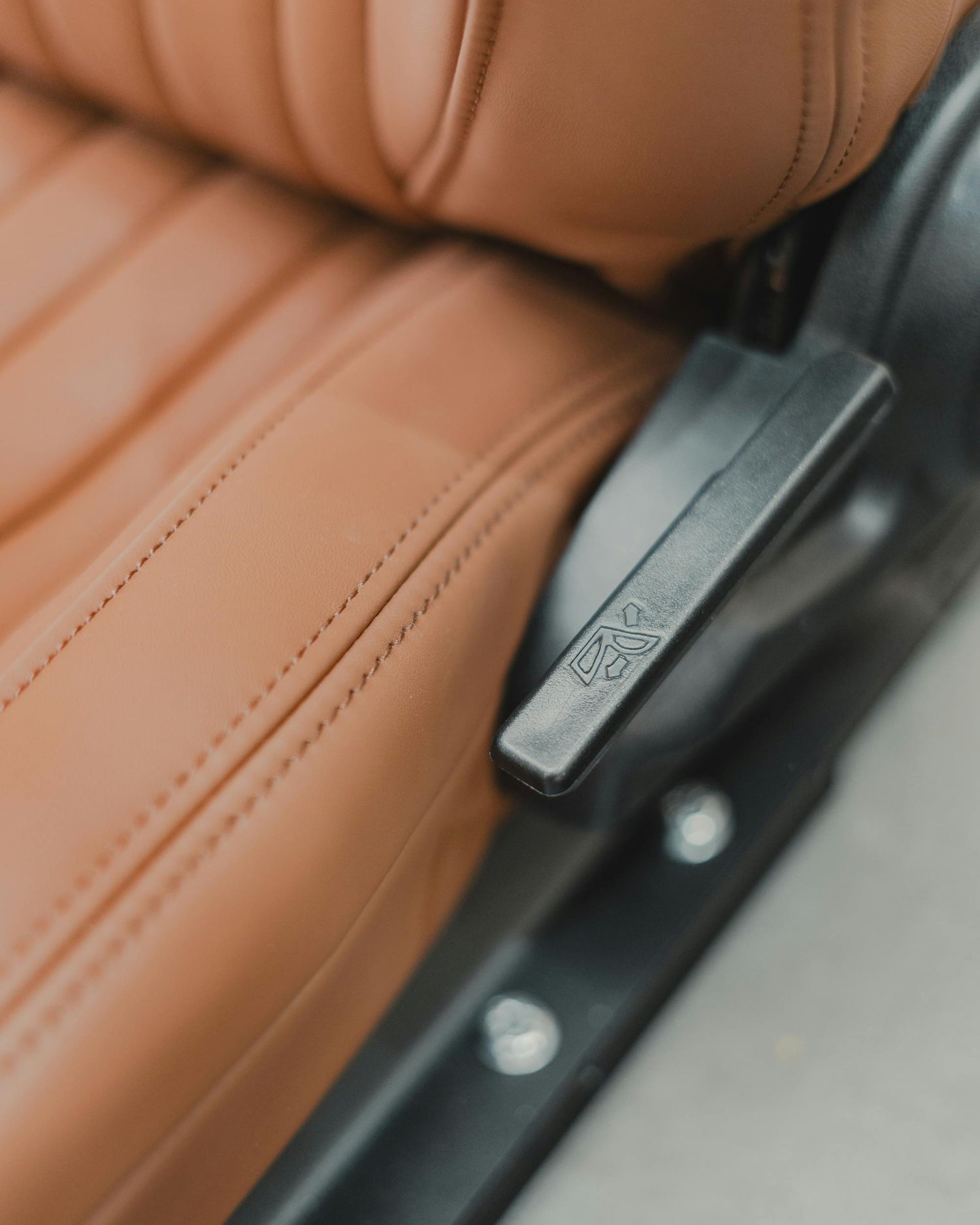 Close-up of a tan leather car seat with a manual adjustment lever, emphasizing the need for protective seat covers to preserve its luxurious finish.